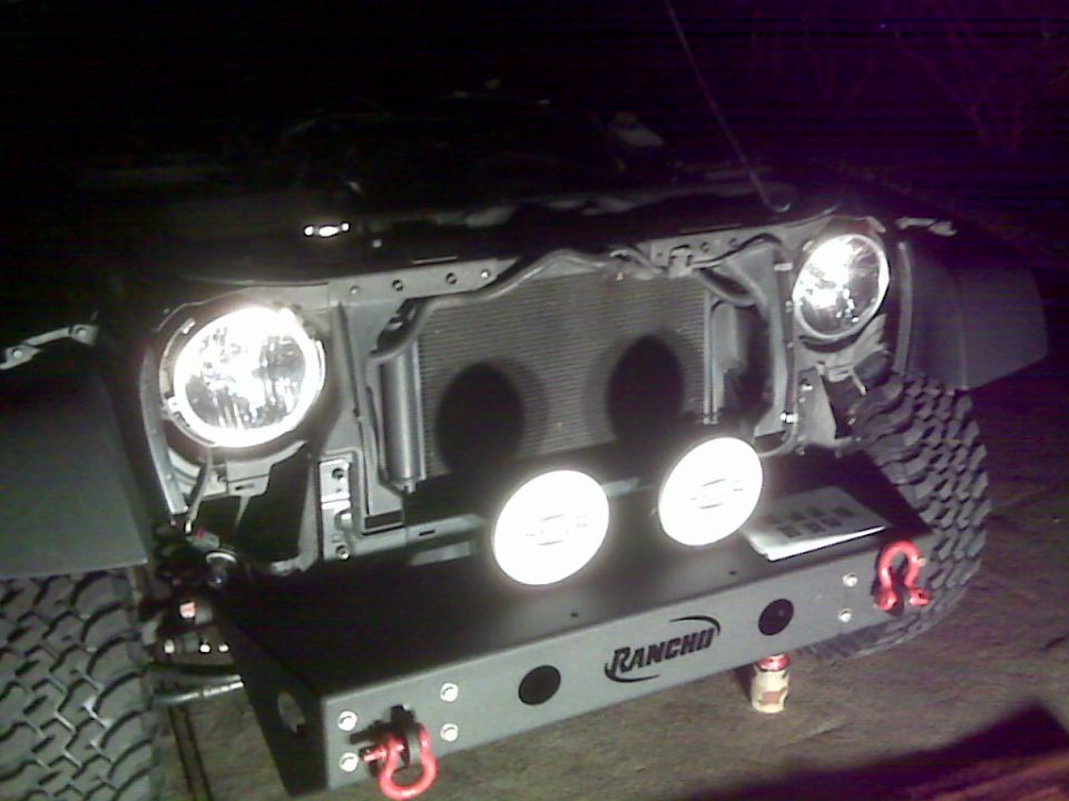 Jeep JK front end at night, grille off, radiator exposed, Rancho bumper with lights on