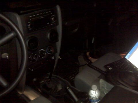 2008 Jeep Wrangler - The interior of a Jeep Wrangler shows the steering wheel, dashboard controls, and a laptop on the passenger seat.
