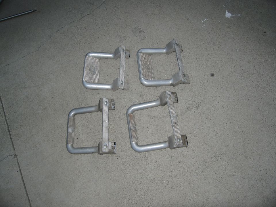 Four metal running boards with textured grip pads are laid out on a concrete surface