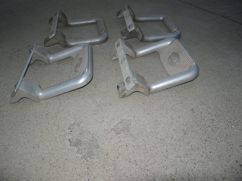 1986 Ford Bronco - Four aluminum running board steps are laid out on a concrete surface, showing their textured grip pads and mounting hardware.