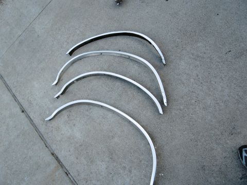 1986 Ford Bronco - Four chrome fender trim pieces are laid out on a concrete surface, likely for sale or restoration.
