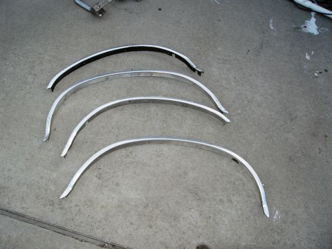 1986 Ford Bronco - Several curved metal trim pieces are laid out on a concrete surface, likely for a vehicle restoration project.