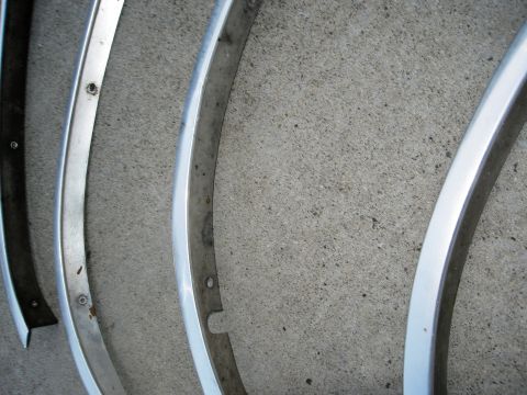 1986 Ford Bronco - Several curved chrome trim pieces are laid out on a concrete surface, showing their condition and mounting details.