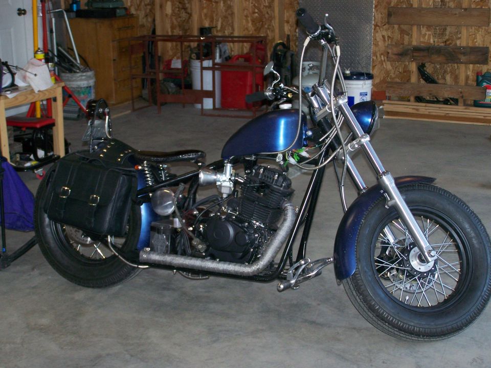 Blue custom motorcycle with black saddlebags and spoked wheels parked in a garage