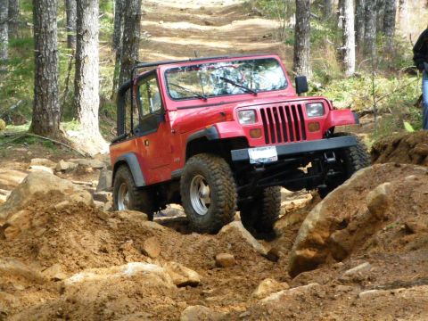 2005 Jeep Wrangler - This red Jeep Wrangler is tackling a challenging off-road course with large rocks and dirt mounds.