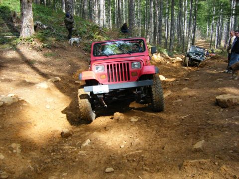 2005 Jeep Wrangler - A red Jeep Wrangler navigates a challenging off-road trail with other vehicles and people present.