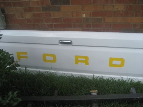 1983 Ford F-250 - The tailgate of a white Ford truck shows the brand name in yellow lettering.
