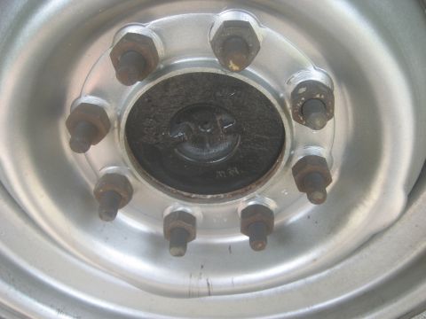 1983 Ford F-250 - A silver wheel hub with eight rusty lug nuts is shown, with a black center cap visible.