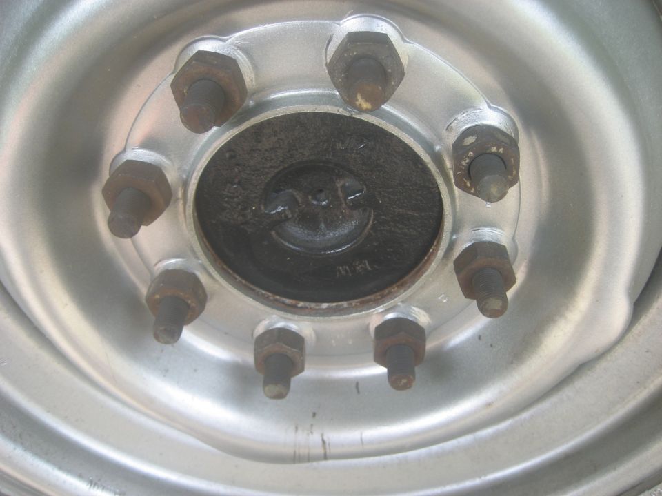 Close-up of a silver wheel hub with eight rusty lug nuts and a black center cap