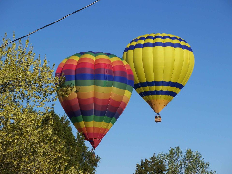 Two hot air balloons, one rainbow-striped and one yellow with blue stripes, against a clear blue sky