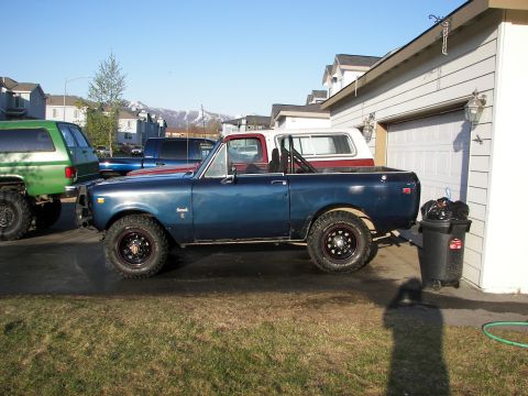 1990 Chevrolet Suburban - A blue pickup truck with a red top and off-road tires is parked in a driveway next to a garage.