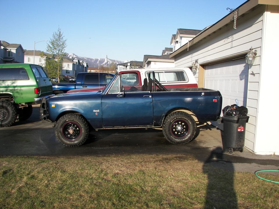 Blue pickup truck with a red top, off-road tires, and a roll bar parked next to a garage