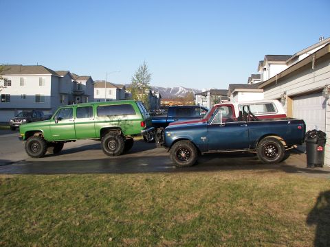 1990 Chevrolet Suburban - A lifted green SUV and a blue pickup truck are parked next to each other in a driveway.