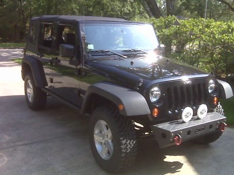2008 Jeep Wrangler - A black four-door Jeep Wrangler Unlimited JK with a black soft top and doors removed, parked on a driveway and shown from the front three-q…
