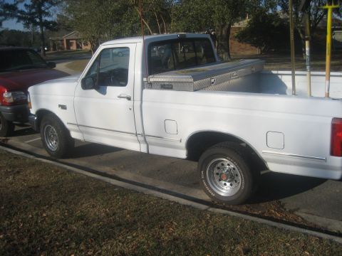 1983 Ford F-250 - A white Ford F-150 pickup truck is parked next to a red vehicle, with gardening tools in the truck bed.