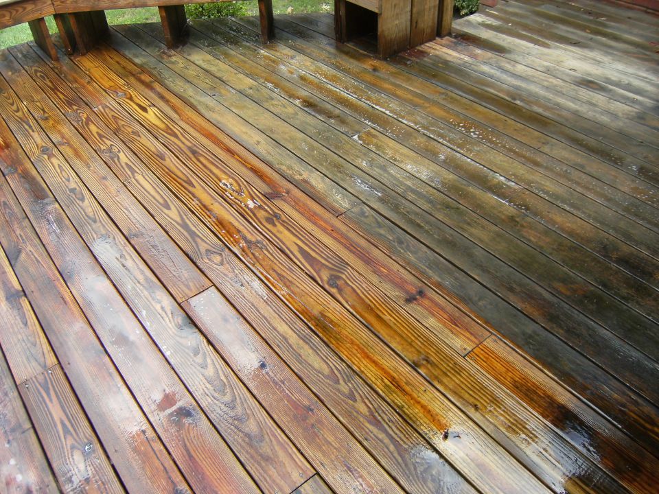 Wooden deck with half cleaned and half dirty planks, wet surface, wooden railing visible