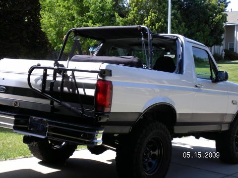1996 Ford Bronco - Lifted white and gray two-tone Ford Bronco with its hardtop removed, folded soft top stowed behind the roll bar and a black swing-out tire…