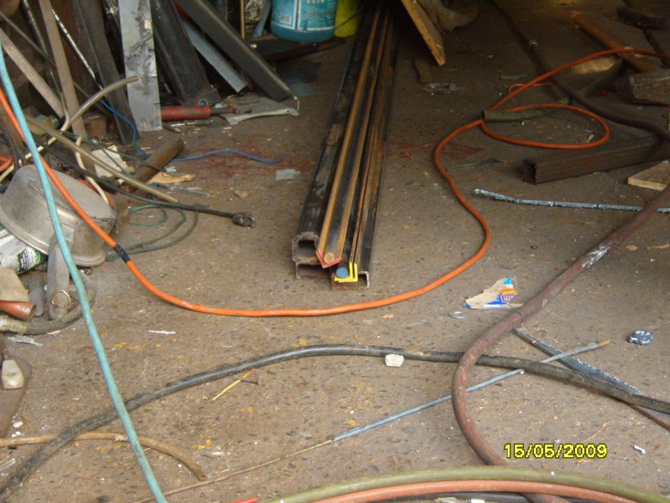 Workshop floor with various metal pipes, hoses, and electrical cords scattered around