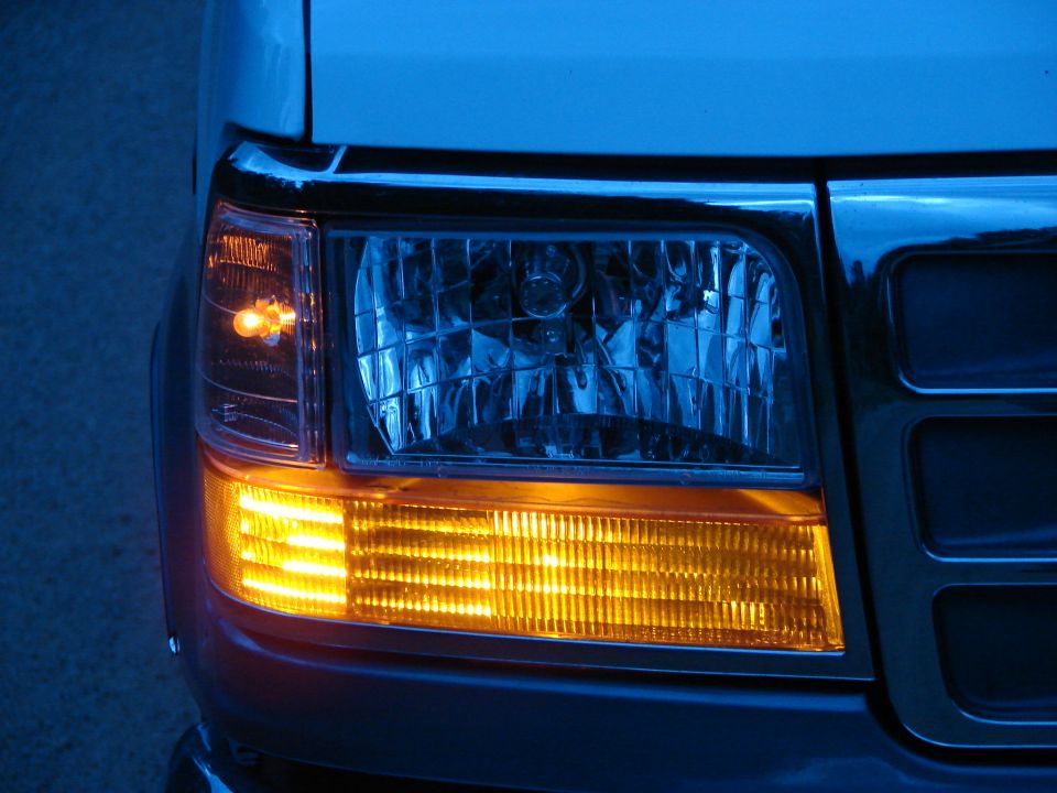 Close-up of a truck's front passenger side headlight and amber turn signal. The turn signal is illuminated