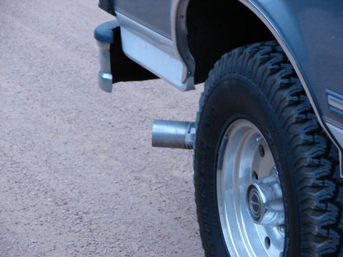 1995 Ford Bronco - Close-up view of a vehicle's exhaust pipe and tire, with a gravelly surface in the background.