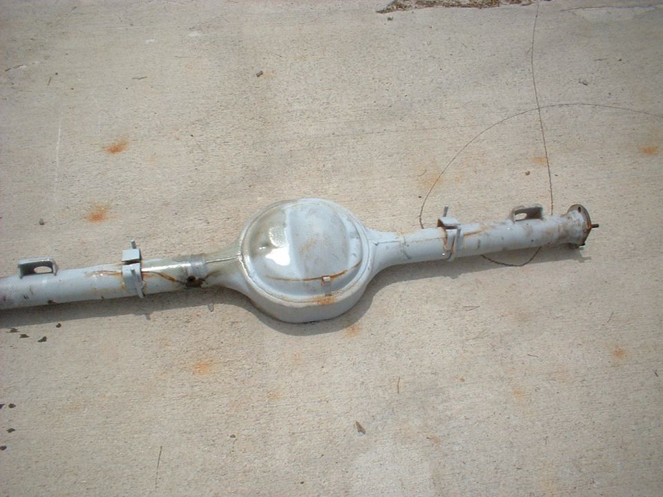 Gray rear axle assembly with a differential housing and two axle tubes, resting on a concrete surface