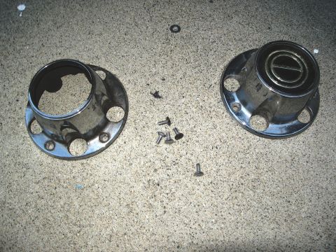 1986 Ford Bronco - Two chrome hubcaps and screws are laid out on a concrete surface. One hubcap has a visible emblem.