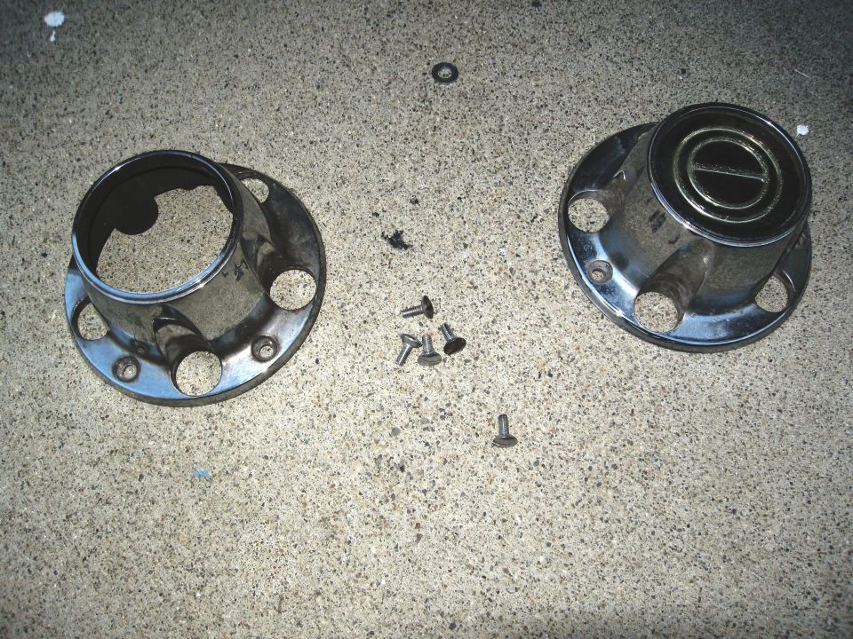 Chrome hubcap with circular emblem and screws on concrete