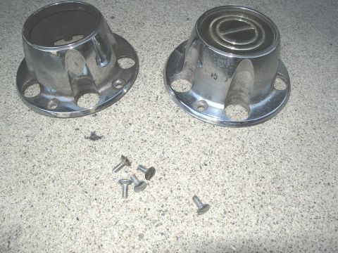 1986 Ford Bronco - Two chrome wheel hubcaps and screws are shown on a concrete surface.
