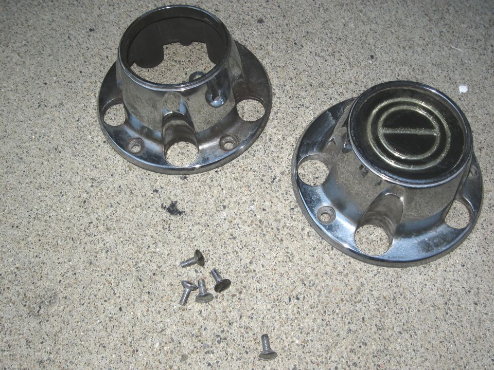 Two chrome hubcaps and screws on concrete