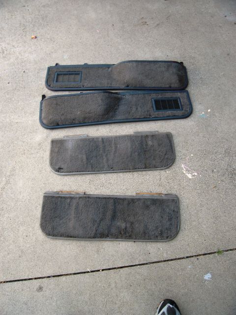 1986 Ford Bronco - Four dark gray carpeted car door panels with vents are laid out on a concrete surface.