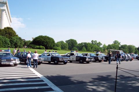 2001 Ford Crown Victoria - Several police vehicles, including sedans and motorcycles, are parked in a lot on a sunny day.