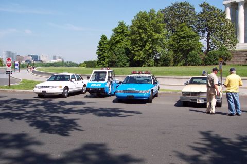 2001 Ford Crown Victoria - Several police and utility vehicles are parked on a street, with a cityscape visible in the distance.