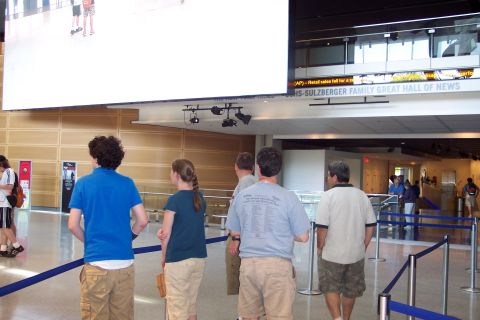 2001 Ford Crown Victoria - People gather in a modern building, observing a large display screen and a scrolling news ticker above an entrance.