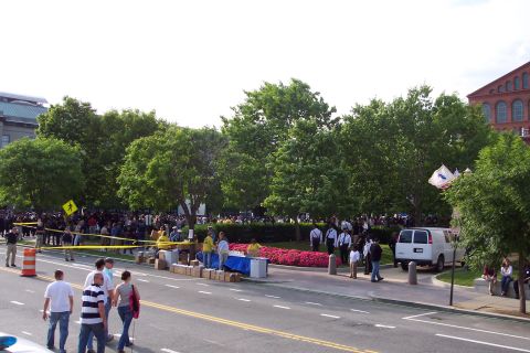 2001 Ford Crown Victoria - A white van is visible on the side of a street with a crowd of people in the background and trees lining the area.