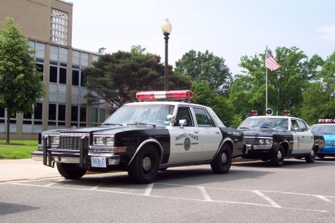 2001 Ford Crown Victoria - Two police cars are parked in a lot, with an American flag visible in the background.