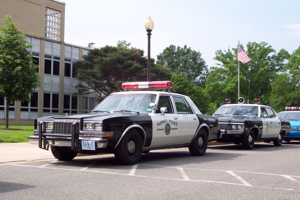 Black and white police car with a light bar, parked in front of a building. License plate reads 169-E