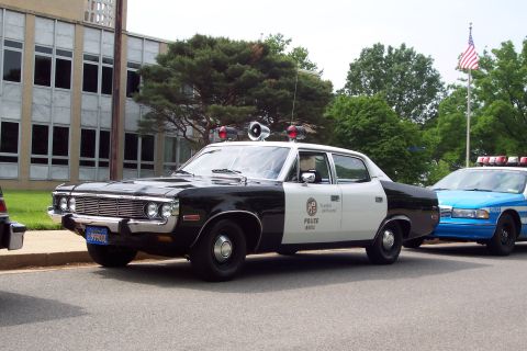 2001 Ford Crown Victoria - A vintage black and white police car is parked on the street next to a modern blue police car.