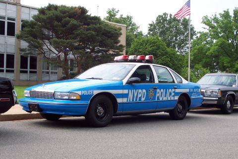 2001 Ford Crown Victoria - A blue and white NYPD police car is parked on a street, with another vehicle to its right.