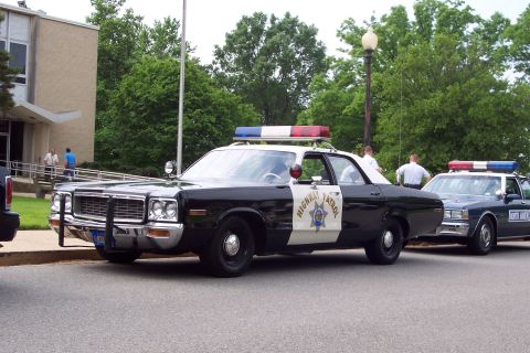2001 Ford Crown Victoria - A vintage police car with a light bar on top is parked next to another police vehicle.