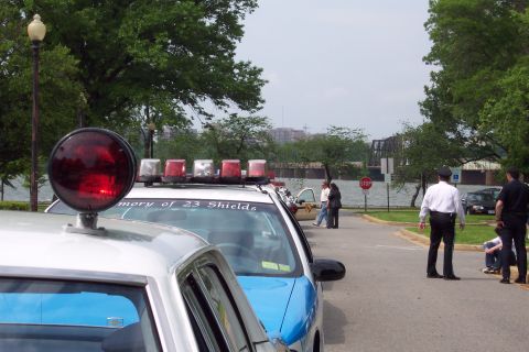 2001 Ford Crown Victoria - Police vehicles are parked near a waterfront with people and a bridge in the background.