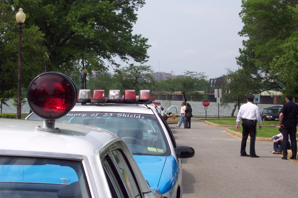 Two police cars parked near a body of water, one with a light bar and text reading 'memory of 23 Shields'
