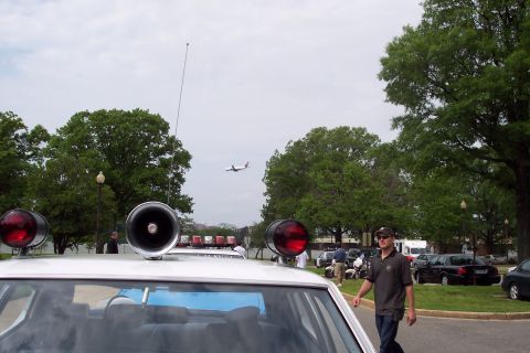 2001 Ford Crown Victoria - A police car is parked outdoors with an airplane in the sky and a man walking past.