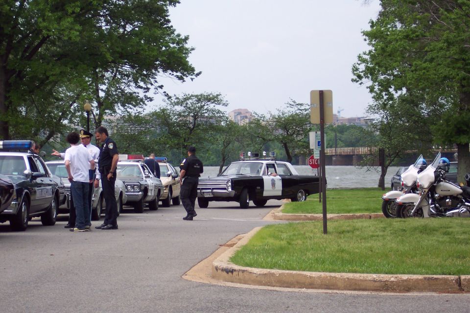 Black and white police car with siren lights, parked on asphalt next to other police cars and motorcycles