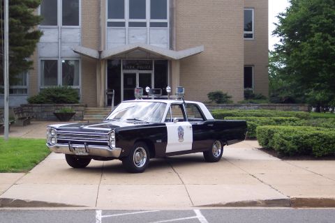 2001 Ford Crown Victoria - This vintage Plymouth Fury police car is parked outside a building with 'PARK POLICE' signage.