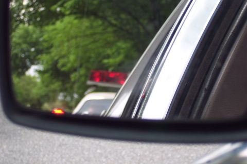 2001 Ford Crown Victoria - Reflection of a police car with flashing red lights seen in the side mirror of another vehicle.