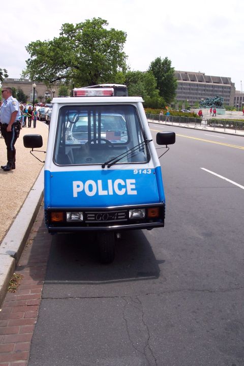 2001 Ford Crown Victoria - A three-wheeled police vehicle, marked 'POLICE' and 'ECO-4E', is parked on the side of a street.