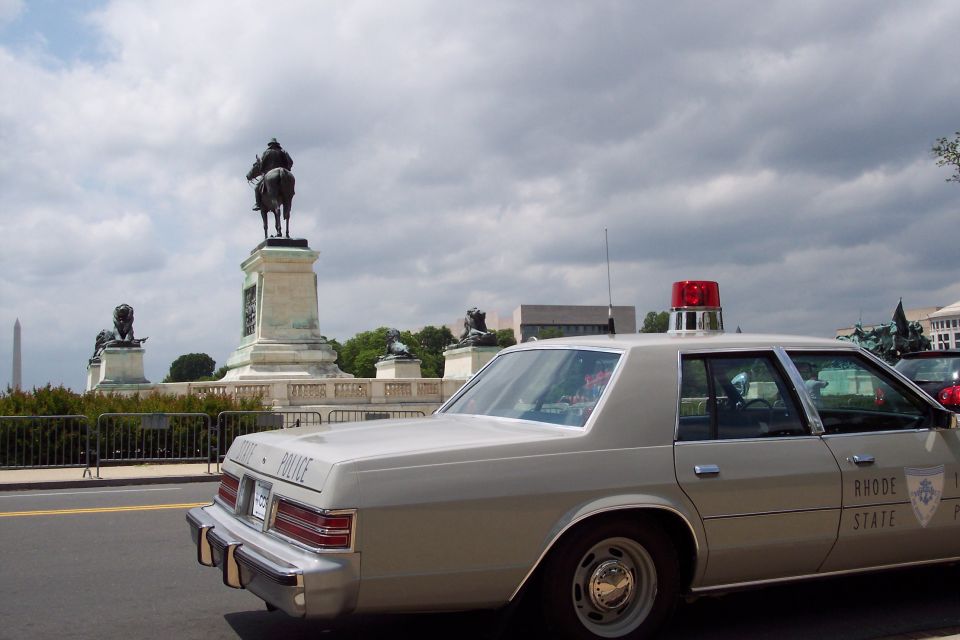 Tan police car with red light bar, side view. Text reads "RHODE ISLAND STATE POLICE"