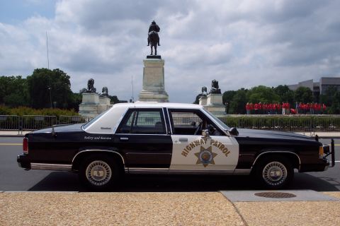 2001 Ford Crown Victoria - Side view of a highway patrol car parked near a monument with a statue on horseback.