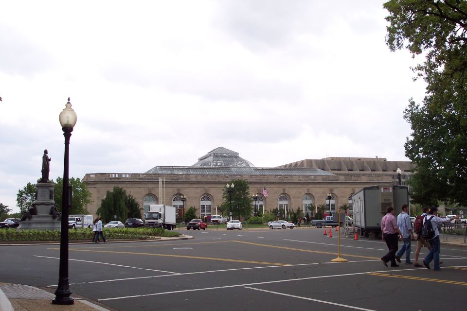 Street view of a large building with a glass dome, several cars, and people walking