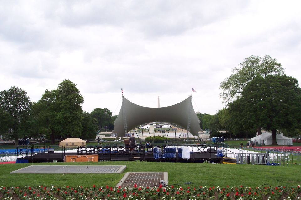 Outdoor stage with a large tent structure, seating, and the Washington Monument in the distance